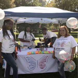Four Black individuals stand in front of a resource fair booth outdoors