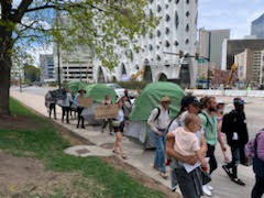 Protesters standing outside camping tents on city sidewalk