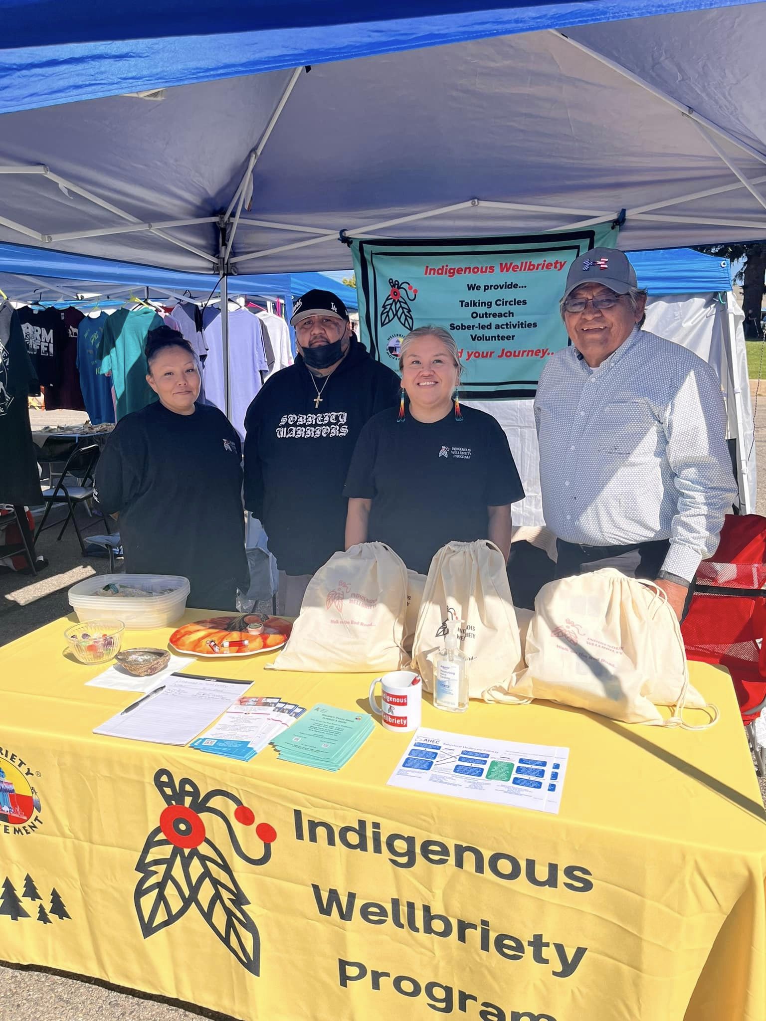 Four people stand in front of a resource fair booth for Indigenous Wellbriety Program