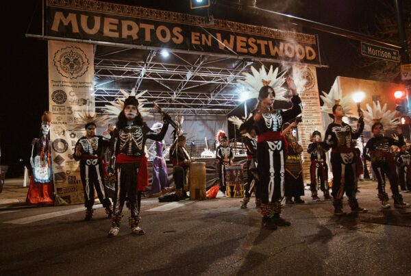 Performers in skeleton outfits on Muertos en Westwood sign