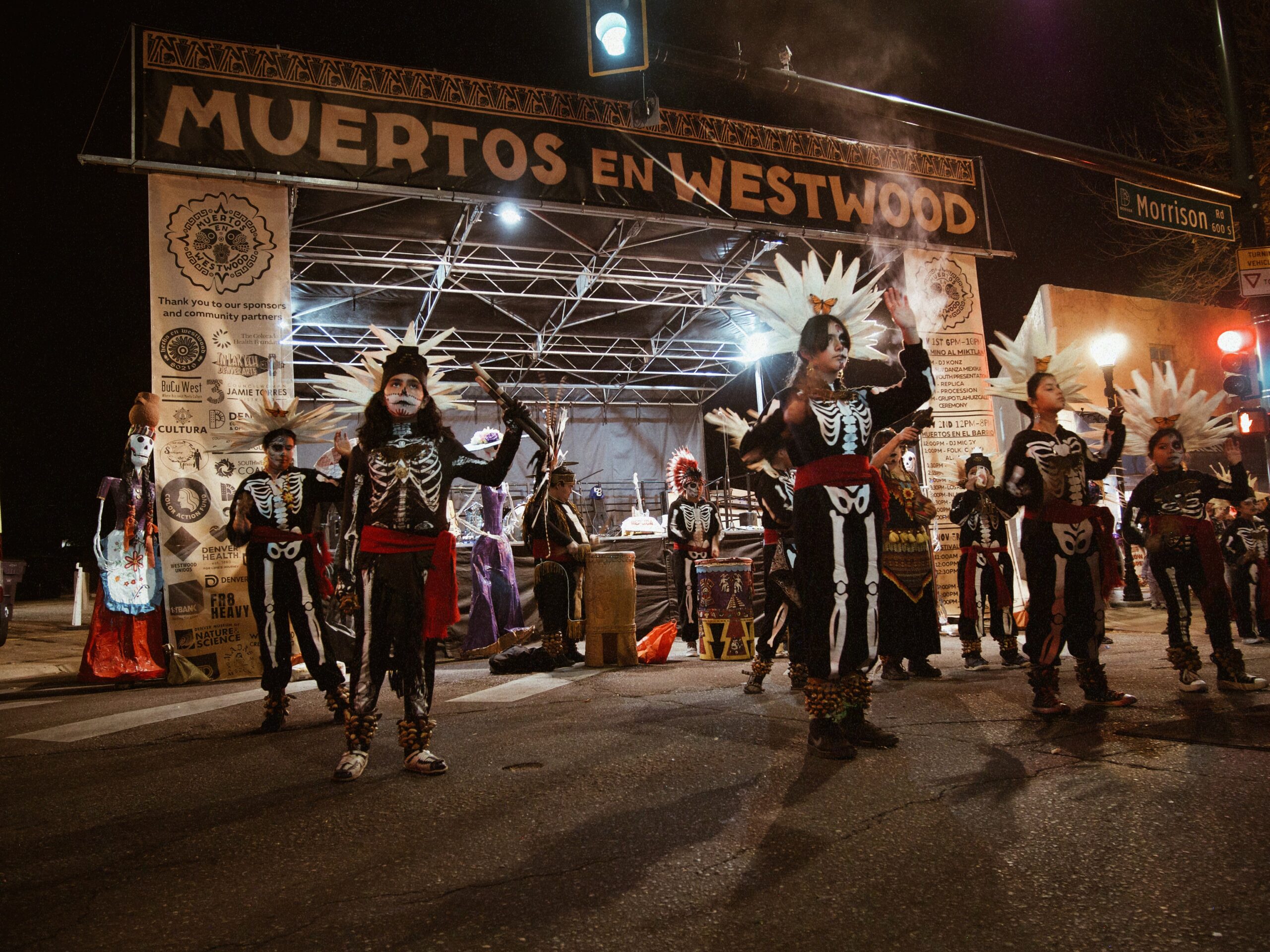 Performers in skeleton outfits on Muertos en Westwood sign