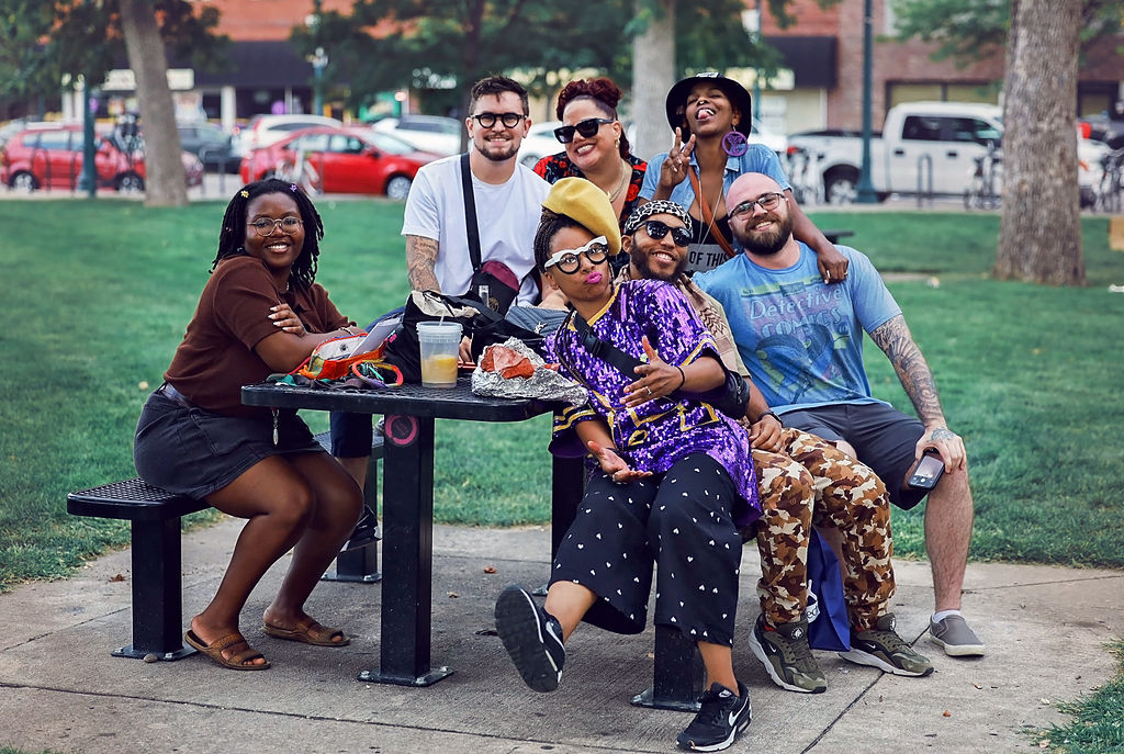 Seven people of color sit together at a picnic table