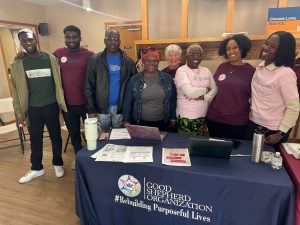 Eight people smiling and standing together behind table