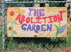 Wooden sign with flowers and the words "The Abolition Garden" painted on in bright colors.