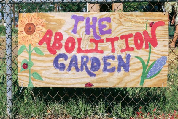 Wooden sign with flowers and the words "The Abolition Garden" painted on in bright colors.